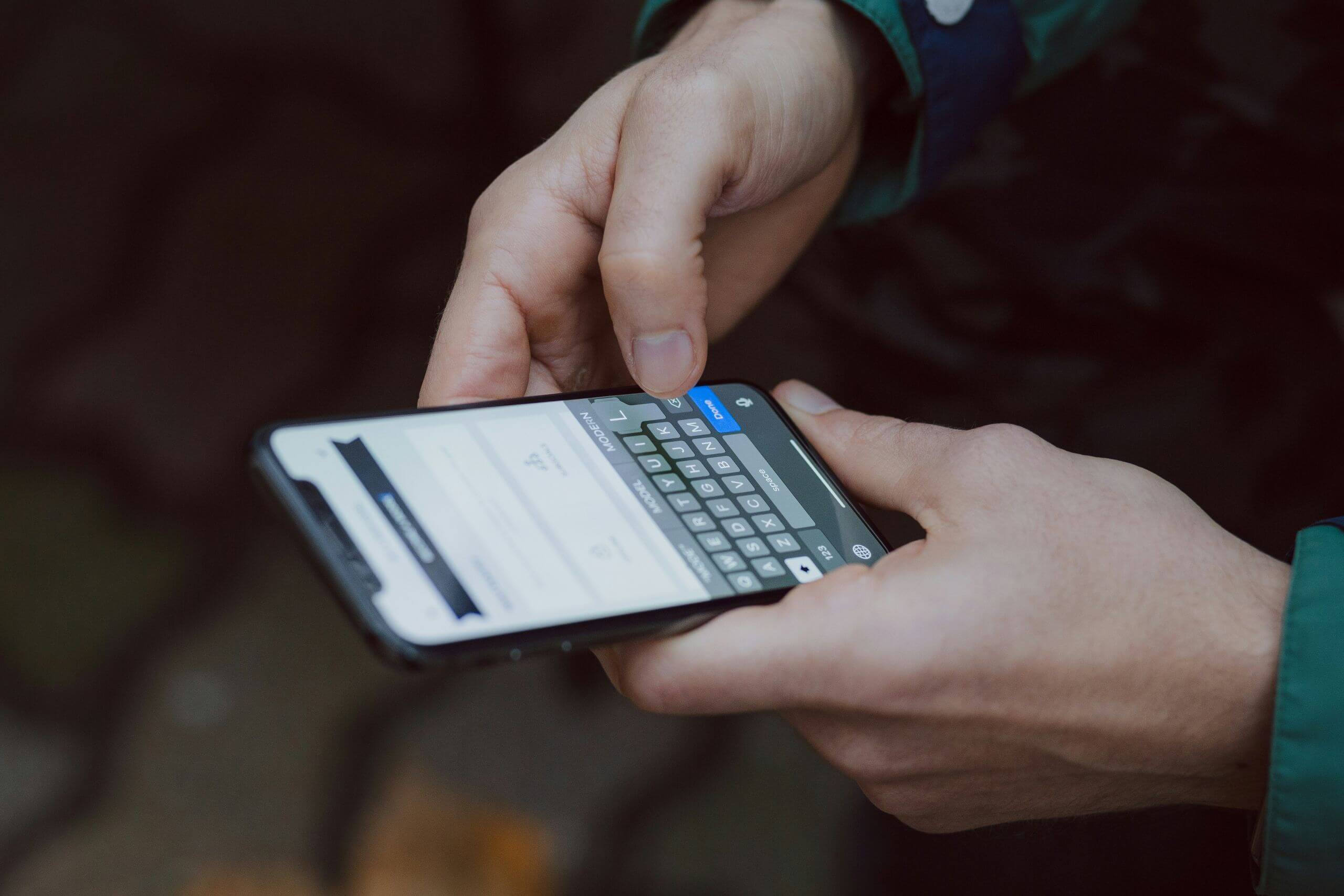 A person holds a smartphone in both hands, typing a message on the touchscreen keyboard. The background is blurred, drawing focus to the phone and hands—raising questions like, "Can the Police Access Your Phone During an Investigation?.