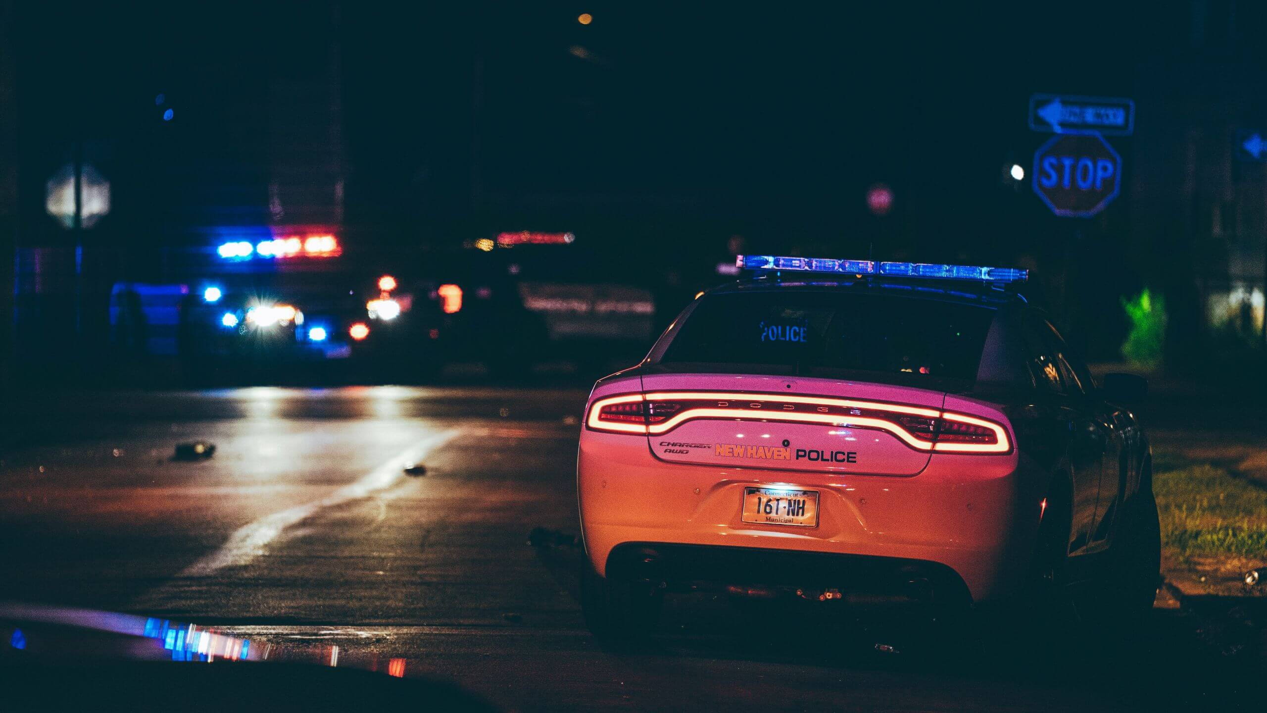 New Haven Police car with its lights flashing at night, parked on the side of the road near a stop sign.