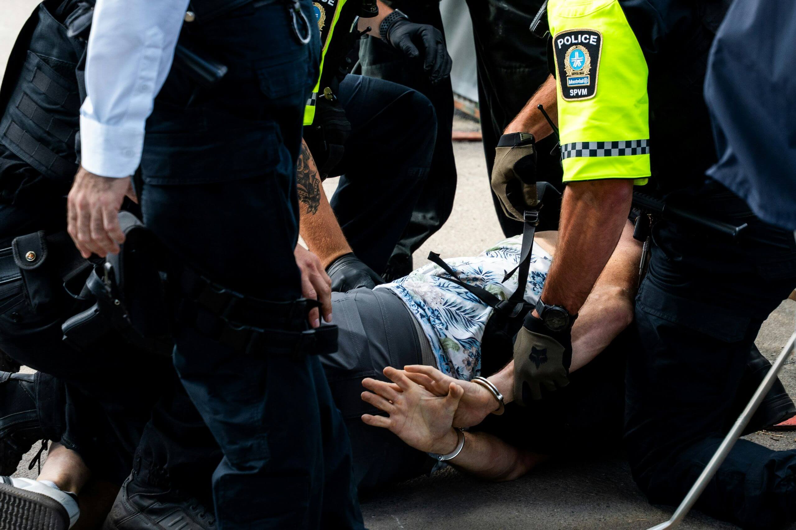 Three police officers in uniform restrain a person face-down on the ground with handcuffs.