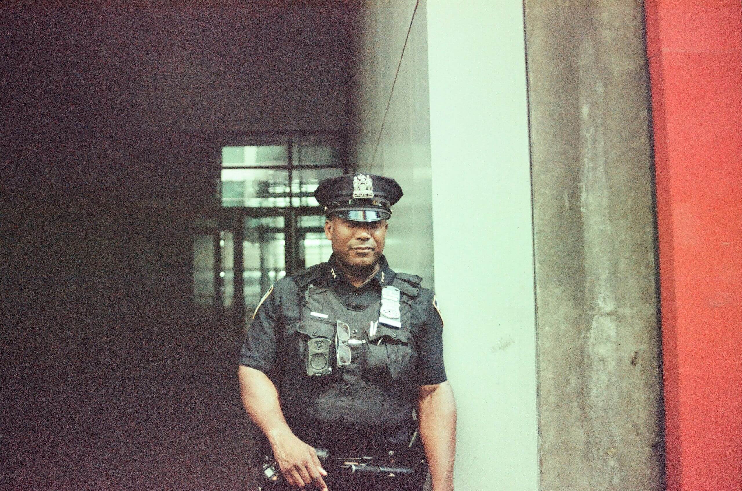 A police officer in a uniform and cap stands in an entryway.